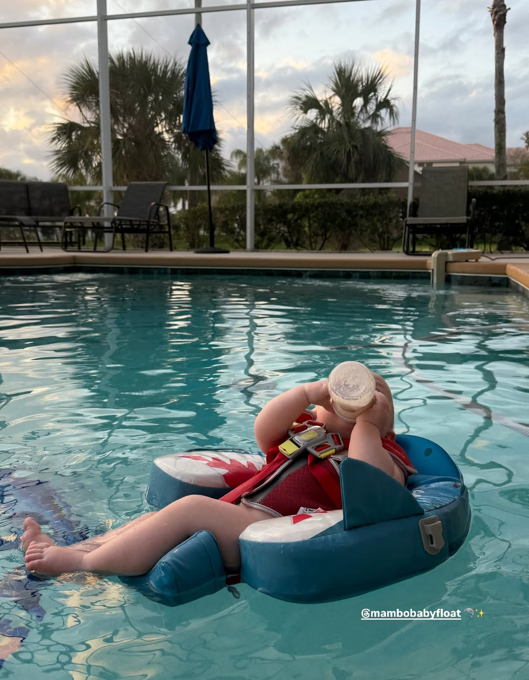 Person lounging on a blue inflatable pool float in a pool with palm trees and a cloudy sky in the background.